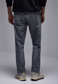 Jeans de mezclilla gris con corte recto, cinco bolsillos y un ligero desgasto. El usuario lleva zapatillas neutrales con acentos claros.