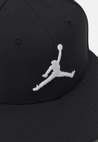 Sort caps i struktureret stof med et hvidt, broderet Jumpman-logo på fronten. Seks-panel design med ventilationsøjel.