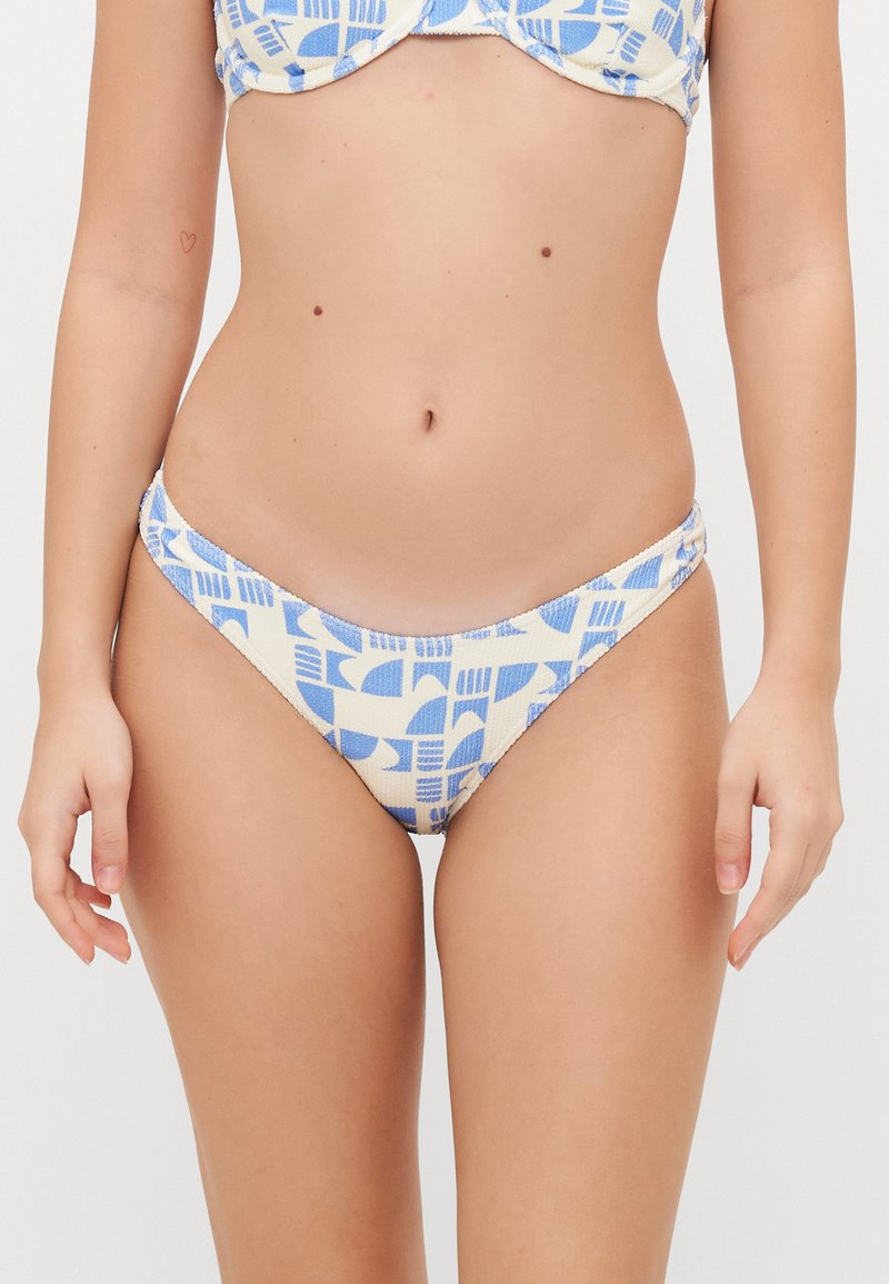 Krém színű bikini alsó, kék geometrikus mintákkal, alacsony szabású és sima textúrájú, oldalán ráncolt részletekkel.