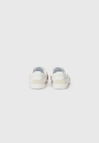 Sapatos casuais brancos com um upper em couro liso e detalhes em camurça bege. Apresenta uma sola texturizada e um design minimalista.