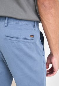 Gros plan d'une personne portant un pantalon bleu clair avec une poche arrière et une petite étiquette orange indiquant BOSS.