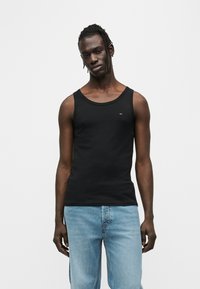 Μαύρο βαμβακερό τοπ χωρίς μανίκια με στρογγυλή λαιμόκοψη, διακοσμημένο με μικρό λογότυπο στο στήθος, συνδυασμένο με ανοιχτό μπλε τζιν παντελόνι.