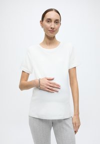 Valge lühikeste varrukatega T-särk ümarate kaelustega, koos helehallide soonikpükstega. Randmel silmapaistev hõbedane käevõru.