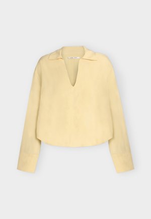 Blusa de manga larga, color amarillo pálido, con escote en V profundo y cuello, que presenta un corte holgado y ligeramente corto.