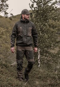 Vandringskläder i mörkgrön och brun, med en zipjacka med lapplagg och matchande byxor; tillverkad av slitstarkt tyg, lämplig för utomhusbruk.