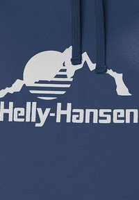 Námořnická modrá mikina s kapucí s bílou grafikou zobrazující hory, vycházející slunce a logo "Helly-Hansen" v tučném písmu. Měkká textilie.