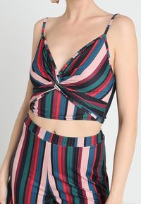 Top bez ramínek, zkrácený s designem ve tvaru twist. Vyrobeno z elastického materiálu s vertikálními pruhy v zelené, růžové, modré a černé barvě.