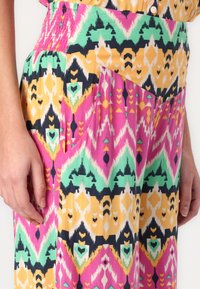 Tessuto colorato con motivo ikat che presenta tonalità di rosa, verde, giallo e blu navy. Vita arricciata e dettagli con tasche visibili. Texture morbida.