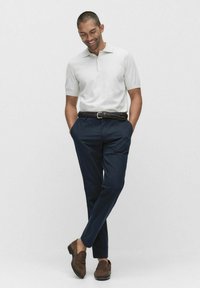 Lichtgrijze polo met korte mouwen, marineblauwe broek, gevlochten bruine riem en bruine suède instappers. Ontspannen pasvorm en casual uiterlijk.