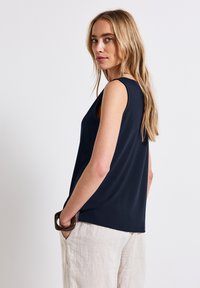 Navy sleeveless top with a relaxed fit, featuring a round neckline and smooth texture. Paired with light-colored linen trousers.