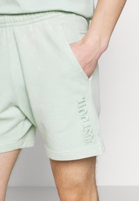Helle grüne Baumwollshorts mit seitlichen Taschen, mit dem in derselben Farbe gestickten Schriftzug "JUST DO IT." Geschmeidige Textur und lockerer Schnitt.