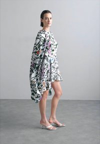 Robe à motif floral avec une silhouette ample et fluide, arborant des accents verts, violets et orange. Tissu mat, ourlet court et manches longues.