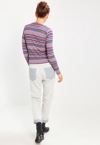 Haut à manches longues rayé en violet, rose et bleu marine ; associé à un pantalon gris clair avec des poches à patch bleues. Les bottes sont noires et brillantes.
