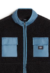 Giacca in pile nera con accenti in nylon blu. Presenta un colletto alto, una cerniera frontale e due tasche sul petto con pattine a scatto.