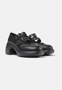 Scarpe in pelle nera con due fibbie regolabili, punta rotonda e tacco spesso e strutturato. Il design include dettagli intagliati sui lati.