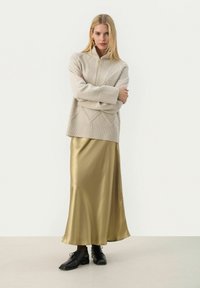 Maglione beige lavorato a maglia con motivi a rombi testurizzati e polsini a coste, abbinato a una gonna maxi in raso dorato lucido e scarpe nere con lacci.