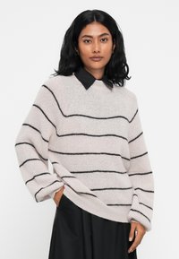 Helle rosa Wollpullover mit schwarzen Horizontalstreifen, runder Halslinie und übergroßen Ärmeln, kombiniert mit einem schwarzen Hemd mit Kragen.