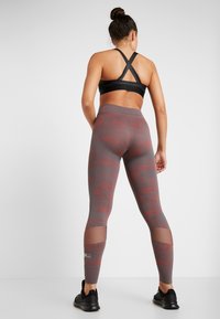 Black sports bra with crisscross back; gray leggings with red camouflage pattern and mesh accents at the calves; black athletic shoes.