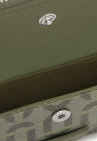 Cartera verde oliva con textura suave, que presenta un cierre de broche plateado y un interior con estampado. El interior tiene costuras finas y un forro suave.