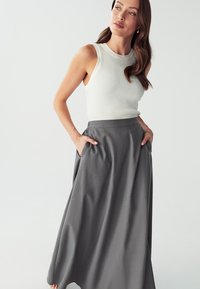 Gray midi skirt with side pockets, made from smooth fabric. Paired with a ribbed white sleeveless top, highlighting a relaxed fit.