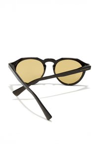 Mustad päikeseprillid ümmarguste kollaste läätsedega, tekstuuriga raam ja sirged mustad sangad. Külgedel on peen logo.