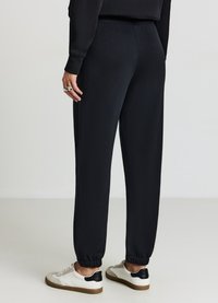 Pantaloni da jogging neri sportivi con polsini e vita elasticizzati, con una texture elegante, abbinati a sneakers bianche con dettagli neri.