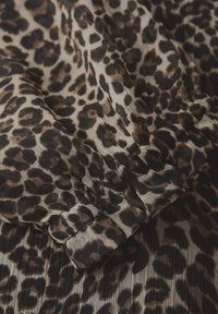 Tessuto maculato leopardato con materiale morbido e texture, in diverse sfumature di beige e nero. Il dettaglio con maniche arricciate aggiunge dimensione e struttura.