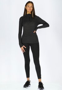 Sort, langærmet sports top med kvart lynlås og tætsiddende sorte leggings lavet af glat stof. Båret med sorte sneakers.