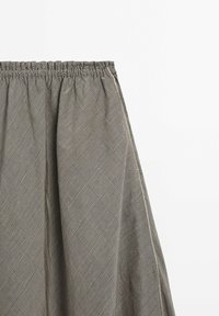 Pantalon à taille élastiquée avec motif à carreaux gris et noir, coupe ample et tissu froncé à la taille sur fond blanc uni.