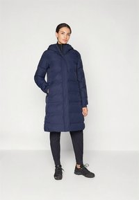 Tengerészkék steppelt kabát kapucnival, cipzáras lezárással, oldalzsebekkel és térdig érő szabással. Sima tapintású és puha párnázattal.