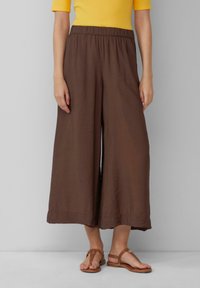 Pantalons larges marron avec une taille élastique, fabriqués en tissu léger, présentant une texture froissée et des ourlets finition.