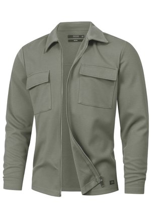 Zielona oliwkowa kurtka na zamek wykonana z mieszanki bawełny, z kołnierzem, długimi rękawami i dwoma przednimi kieszeniami na piersi. Tkanina o fakturze.