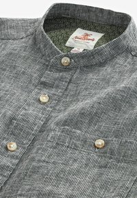 Grå knäppt skjorta med vitt rutmönster, beige knappar och mönstrad innersöm i kragen, vikta så att framsidan och krags detaljer syns.