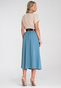 Beżowa bluzka z krótkim rękawem z ozdobnym zapięciem z tyłu, połączona z lekko opadającą niebieską spódnicą midi, podkreślona czarnym paskiem i sandałami na obcasie.