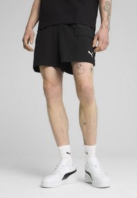 Shorts de sport noirs avec poches latérales et un logo Puma blanc, associés à des baskets blanches avec des accents noirs et des chaussettes côtelées.