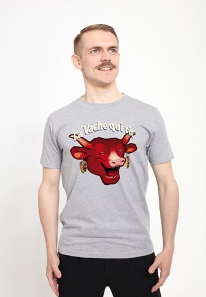 Šedé bavlněné tričko s velkým červeným obrázkem usmívající se krávy s náušnicemi a textem "La Vache qui rit" nahoře. Standardní kulatý výstřih.