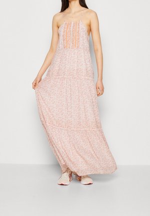 Maxi-jurk met dunne bandjes, zachte roze basis, wit bloemenpatroon, gestructureerde voorkant, gelaagde zoom, gecombineerd met lichte sportschoenen.