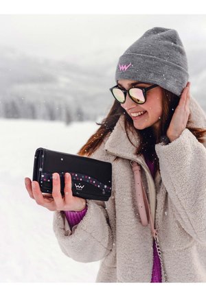 Black wallet with colorful polka dot design, held in a person's hand, alongside a cream fleece jacket and gray knit beanie with logo.