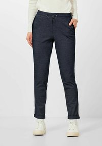 Donkerblauwe broek met een gestructureerd patroon, elastische tailleband, verstelkoord, zijzakken en opgerolde mouwen, gecombineerd met witte sneakers.