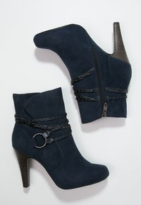 Marinblå mocka ankelskor med spetsig tå, hög klack, dekorativa kedjeaccentuer, och dubbla dragkedjor på utsidan.