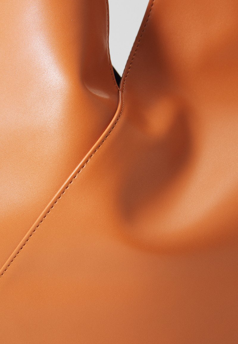 Close-up of smooth, tan leather with detailed stitching and a slight indentation near a central curved seam.