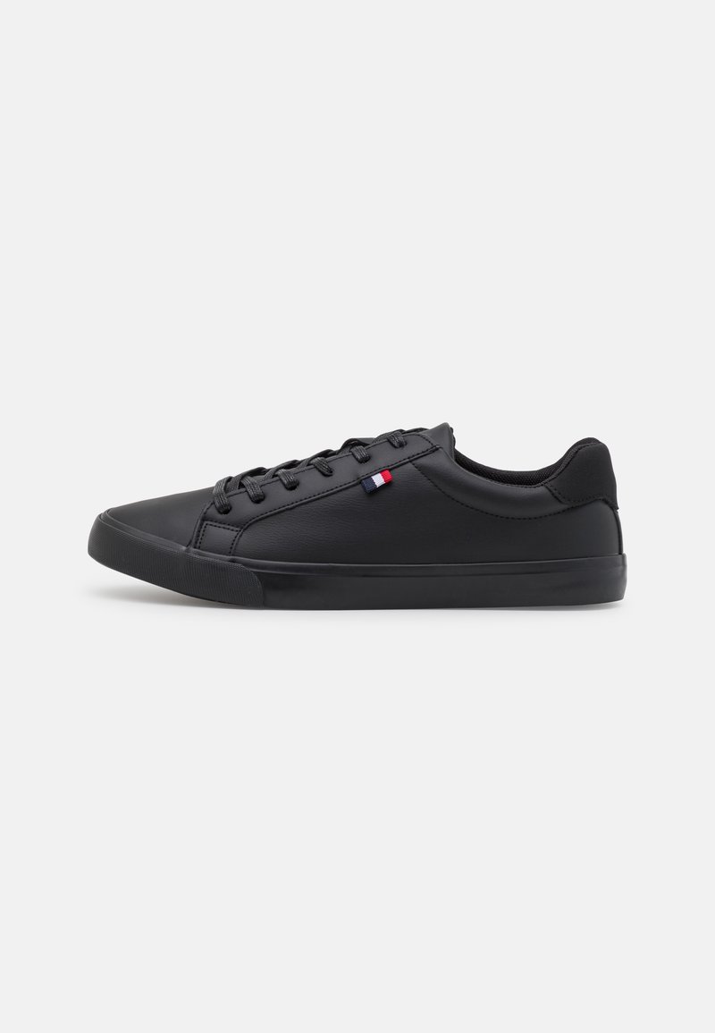 Baskets basses en cuir noir avec lacets noirs et un petit détail de drapeau rouge, blanc et bleu sur le côté.