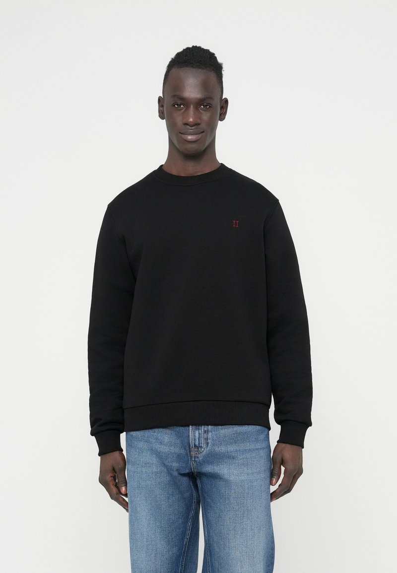 Juodas džemperis pagamintas iš minkštos medžiagos, su apvalia apykakle ir ribotomis rankogaliais. Ant krūtinės yra mažas raudonas "II" logotipas. Derinamas su mėlynomis džinsomis.