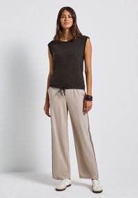 Černý top s krátkým rukávem, lehký materiál, v kombinaci s béžovými kalhotami s širokými nohavicemi a černými bočními pruhy. Celý vzhled doplňují casual bílé tenisky.