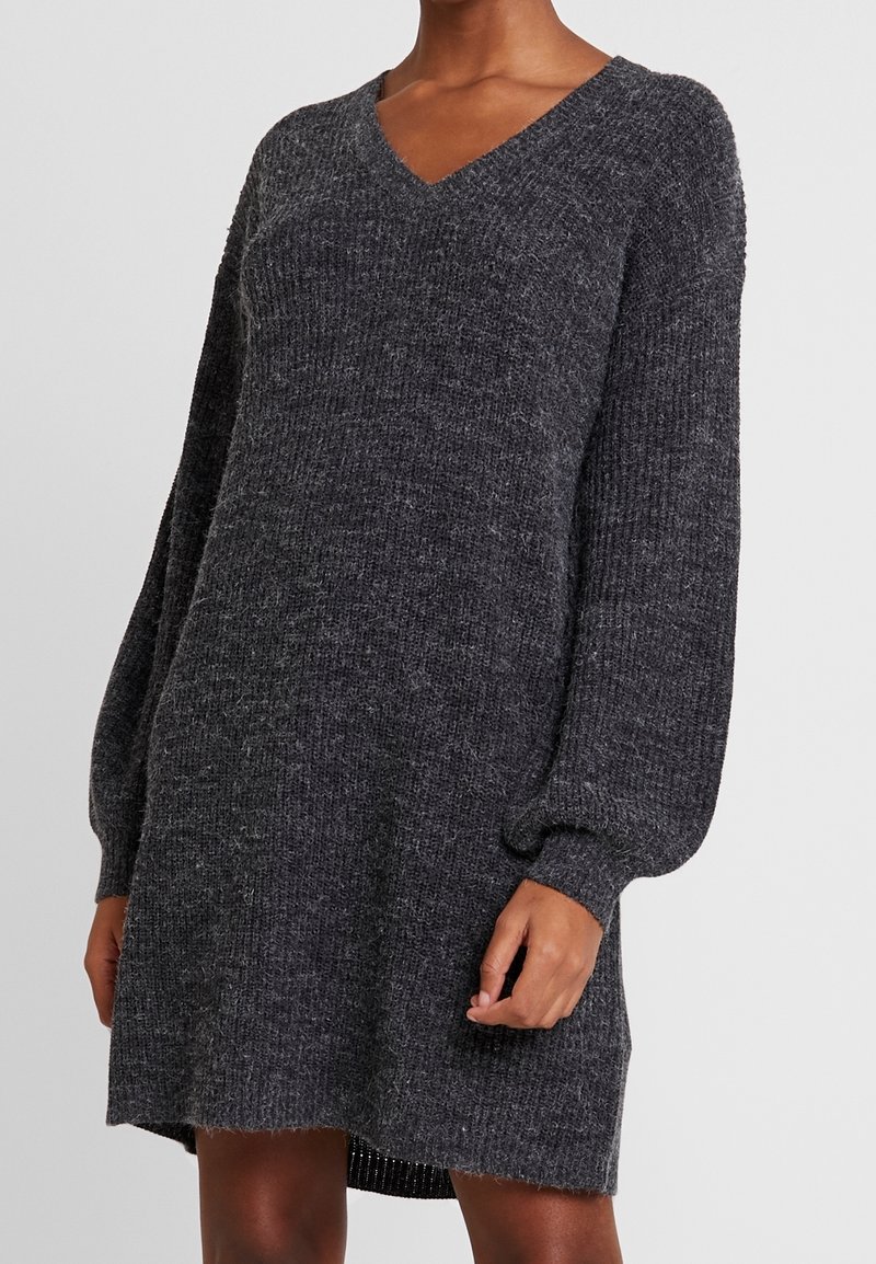 Robe-pull en maille côtelée gris foncé avec manches longues ballon et décolleté en V, portée par une personne à la peau brune.