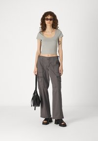Sivi kroj fit majica, široke sive cargo hlače s džepovima, crne platforme sandale i mala crna torba. Glatke teksture kroz cijeli outfit.