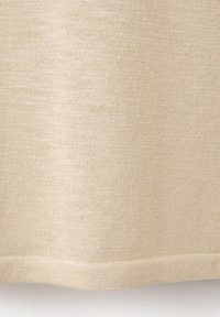 Tissu beige en maille avec une texture fine et des coutures horizontales visibles près du bord inférieur du matériau.