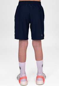Marineblauwe sportshorts met een elastische tailleband, zijzakken en een gladde textuur. Gepaard met witte sokken en schoenen met een oranje accent.