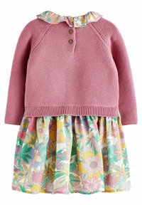 Vaaleanpunainen neulepaita, jossa on kolme nappia kauluksessa, sekä kerroksellinen kukkakuosisessa hameessa pastelivärejä ja vihreitä yksityiskohtia.