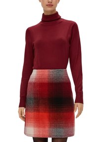 Burgunderfarbener Rollkragenpullover kombiniert mit einem rot-schwarzen Karorock. Der Rock hat abwechselnde farbige Quadrate in unterschiedlichen Größen.